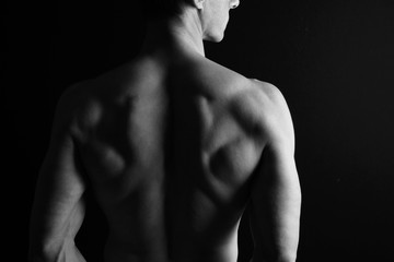 Strong muscular athletic man back on dark background, low key image, copy space