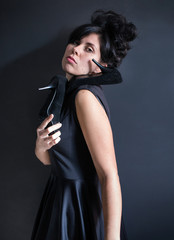 photo dark haired model in black dress with a high hairdo holding a high heeled shoes