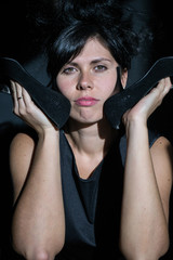 photo portrait of a woman in black with a high hairdo holds shoes at the face to the cheeks heels