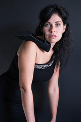 portrait of a dark haired model in black dress on one shoulder and a shoe with a heel