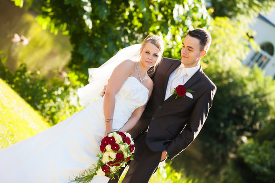 sehr junges Paar auf dem Hochzeitsfoto nach der Hochzeit in weiß mit schönen roten Rosen Blumenstrauss