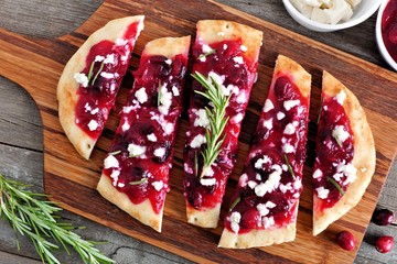 Festive flatbread appetizer with cranberries and goat cheese, overhead scene on a serving board against rustic wood