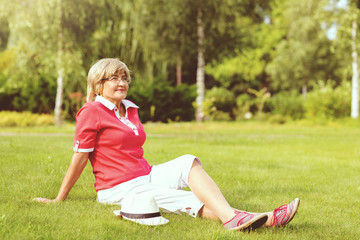Portrait of happy smiling senior woman sitting on a grass outside on sunny day