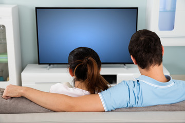 Couple Sitting On Sofa In Front Of Television