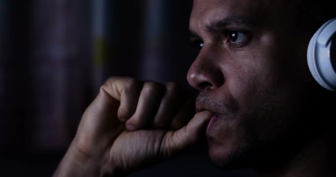 4K Man at night with headphones watching a screen and biting his nails
