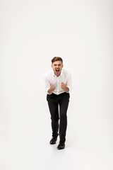 Young successful businessman in suit shouting over white background.