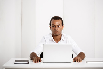 Young successful african businessman sitting at workplace with laptop.