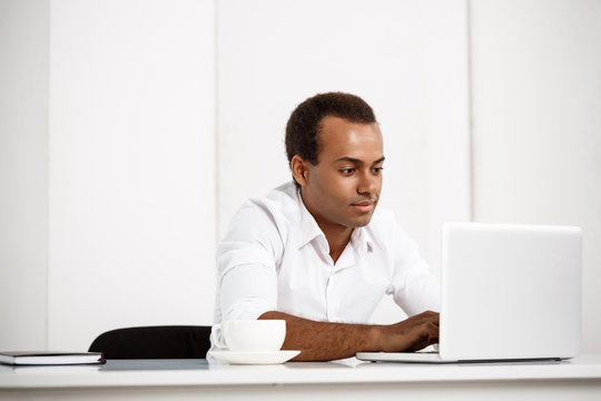 Young successful african businessman typing on laptop, sitting at workplace.