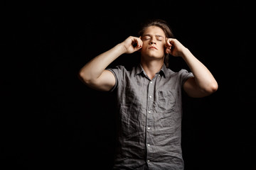 Young handsome man thinking with closed eyes over black background.