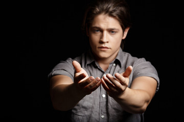 Young handsome man stretching hands to camera over black background.