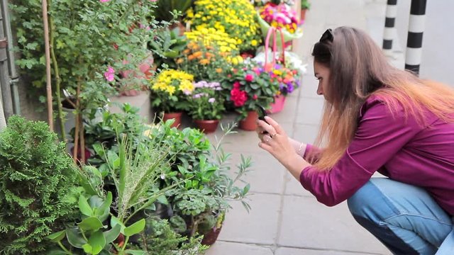 Young woman photographing flowers in a small flower shop on the street in Europe