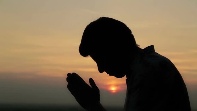 Silhouette of young man praying at sunset. Sunset light, golden hour. Religion, spiritual and nature concept