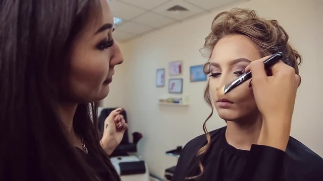 Make up artist doing professional makeup of young woman in beauty studio