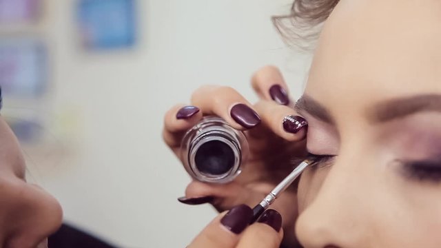 Make up artist doing professional eye makeup of young woman