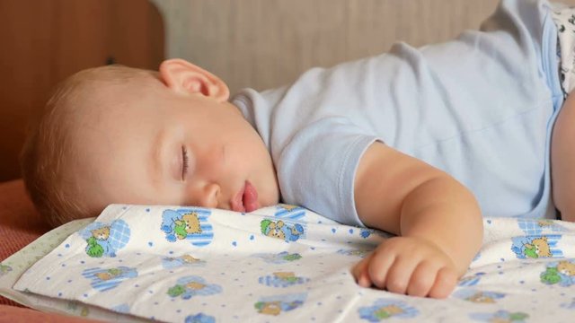 Beautiful baby sleeping in funny pose on a bed. Under the baby diaper, the boy about a year