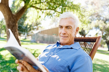 Senior man sittingin park while reading book