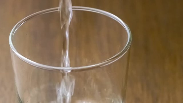 Clean clear filtered water being poured into drinking glass against dark wood background, slow motion 30p