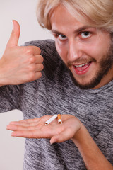 Man with broken cigarette on palm making thumb up