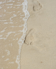 Footprint in the sand and small wave