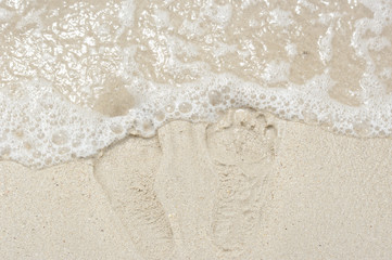 Fototapeta na wymiar Footprint in the sand and small wave