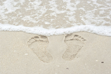 Fototapeta na wymiar Footprint in the sand and small wave