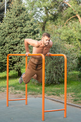 Fototapeta premium young man doing triceps dip on parallel bars outdoors