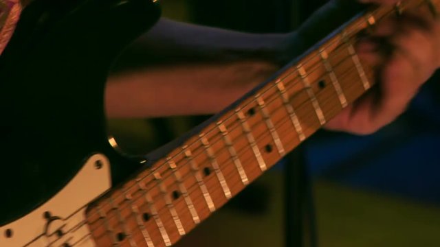 Closeup Hand Touches Electric Guitar Strings in Night Bar