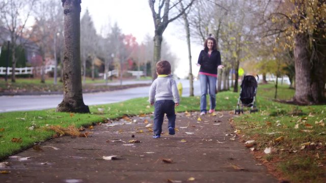 Adorable little boy walking toward his mom in a park on a fall day