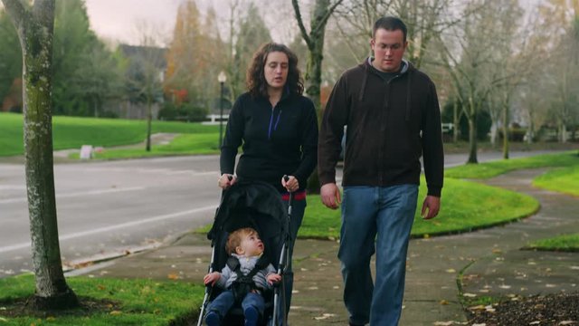 Parents on a walk pushing their little boy in a stroller, on a fall day