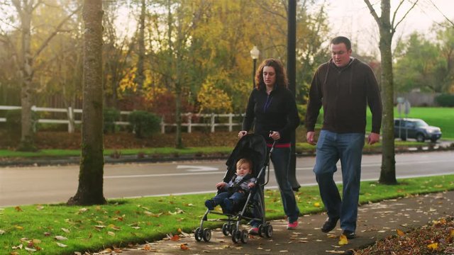 Parents on a walk pushing their little boy in a stroller, on a fall day