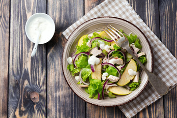 Salad with lettuce, apple, celery, onion and chicken on the gray plate on dark wooden background.Selective focus.Top view.