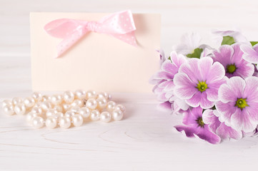 Fototapeta na wymiar Bouquet of violet primroses with paper greeting card and pearl necklace