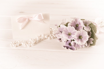 Bouquet of violet primroses with greeting card and pearl necklace