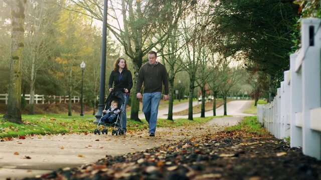 Parents on a walk pushing their little boy in a stroller, on a fall day