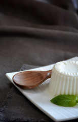 fresh cheese with basil leaves on a white plate and a table with