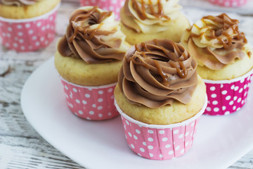 Vanilla cupcakes with a cap of cream on white wooden table