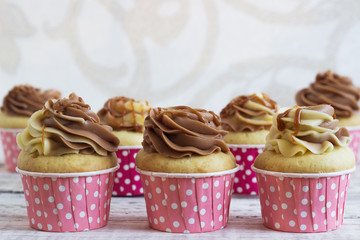 Vanilla cupcakes with a cap of cream on white wooden table