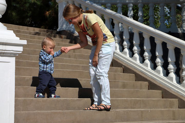 Baby in a plaid shirt making his first steps on a ladder, mother holding his hands supporting by learning to walk