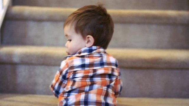 Little boy standing at the bottom of stairs, holding a sippy cup