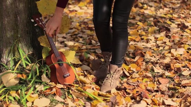 Young Beautiful Girl Playing Ukulele Guitar and Singing in Autumn Nature Under Yellow Tree. Ukulele concept. Selective focus.