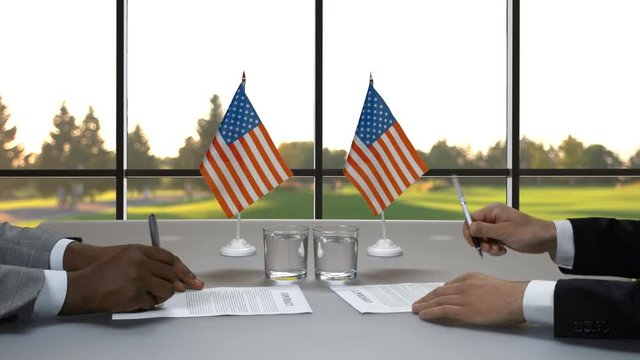 Businessmen signing papers at desk. Men shaking hands near flags. Politicians in USA. Both sides agree.