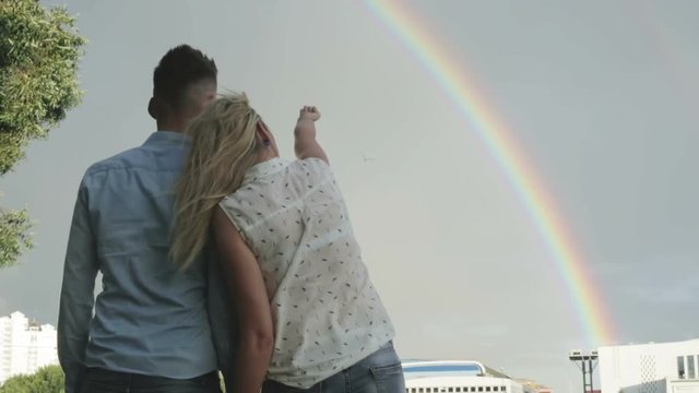 A girl showing a rainbow in the sky to her boyfriend.