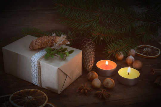 Eco Christmas packages gift and two light candles with Christmas and New Years decor and Christmas tree on dark wooden background