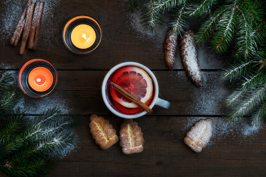 Hot tea with lemon and cinnamon in white cup. Two light candles, Christmas tree and cookies on dark wooden background. Top view.