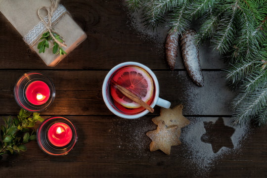 Hot tea with lemon and cinnamon in white cup. Eco Christmas packages gift. Two light candles, Christmas  tree and cookies on dark wooden background. Top view.