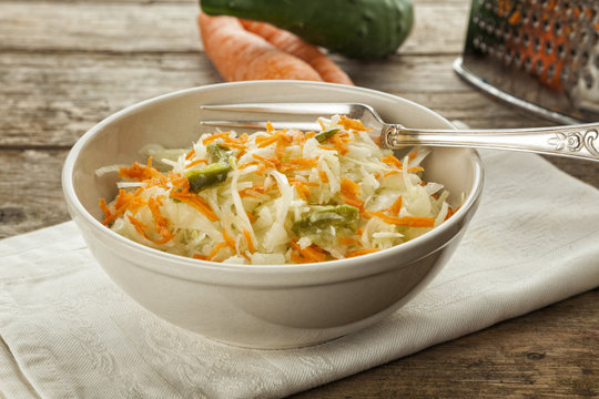 Coleslaw in bowl on table, grater and vegetables in background