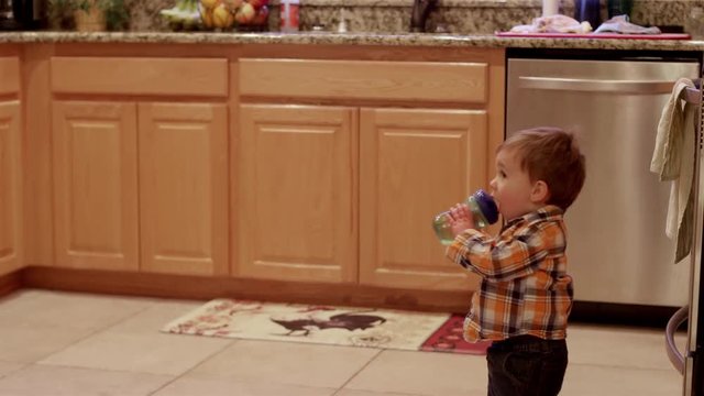 Little boy in a kitchen gets a sippy cup handed to him and walks out