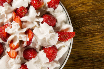 Strawberry with chantilly cream in a dish on a wooden table