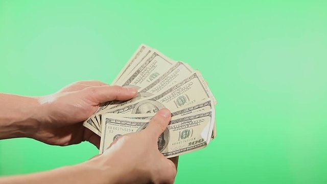 Close up of hands counting various united states dollar notes over green background.