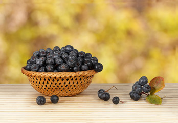chokeberry in a wicker basket on a wooden table on a background of red leaves